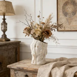 Abstract human face ceramic vase in a rustic interior setting with dried flowers.