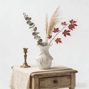 Dettaglio di vaso in ceramica bianca con rilievi e fogliame autunnale essiccato