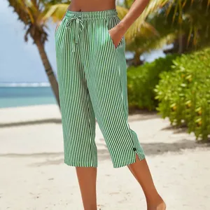 Close-up detail of green and white striped cropped pants with drawstring waist on a beach.