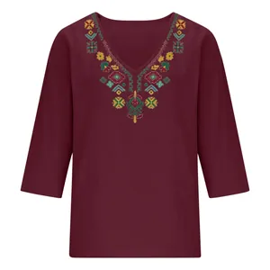 Detail of intricate colorful ethnic embroidery on a burgundy cotton linen V-neck top.