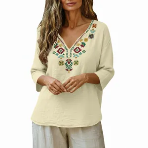 Close-up detail of bohemian embroidered neckline on a loose cream cotton linen V-neck blouse