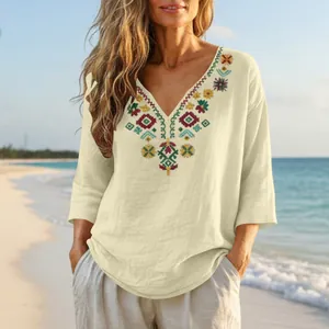 Detail of boho embroidered linen top with V-neck and 3/4 sleeves on beach background.