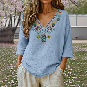 Detail view of colorful bohemian embroidery on light blue V-neck cotton linen top.