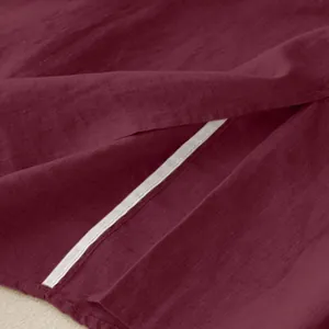 Macro detail of burgundy linen midi skirt showing the side slit and fabric texture.