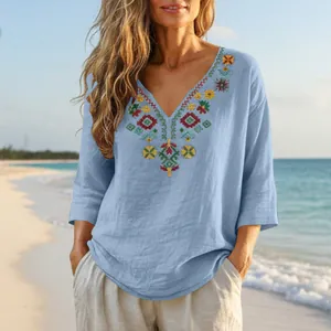 Detailed view of boho V-neck cotton linen blouse with colorful embroidery on a beach
