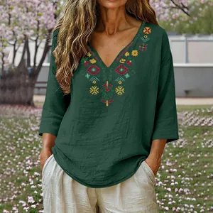 High-quality detail of vintage ethnic embroidery on a green V-neck linen blouse.