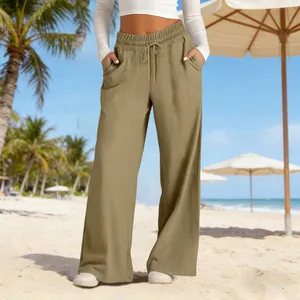 Close-up detail of high-waisted wide-leg trousers in olive green on a sunny beach