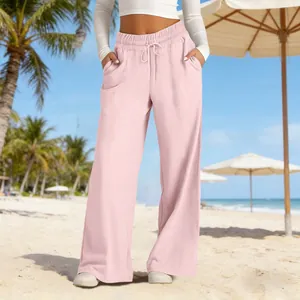 Stylish women's pink high-waisted wide-leg trousers shown in a sunny beach resort setting