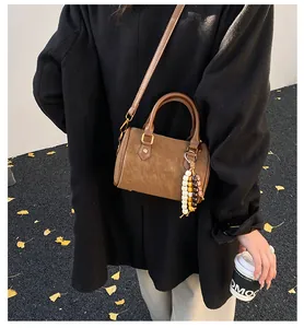 Lifestyle-Detail einer braunen Vintage-Boston-Tasche mit Perlenanhänger und schwarzem Mantel.