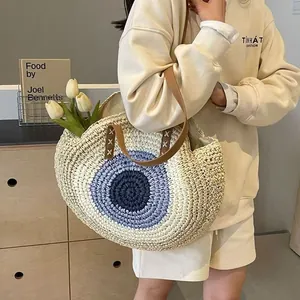 Fashionable bohemian woven round straw shoulder bag with evil eye design on model
