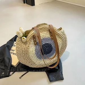 Detail view of a circular woven straw beach bag with purple eye pattern and brown straps