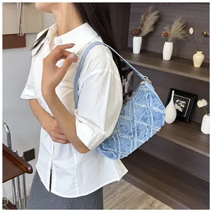 Model wearing a light blue denim underarm bag with frayed diamond pattern details