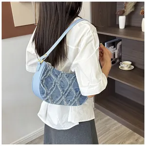 Detail of light blue denim underarm bag with quilted diamond pattern and frayed edges.