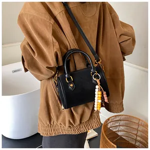 Detail einer schwarzen Boston-Tasche mit Holzperlenquaste und einer braunen Jacke