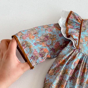 Infant floral romper sleeve detail close-up, blue vintage print fabric with brown trim ruffles.