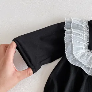 Baby rompers detail shot, black long sleeve with white lace ruffle collar closeup.