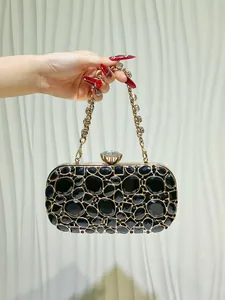 Elegante pochette da sera con strass neri e catena dorata tenuta in mano