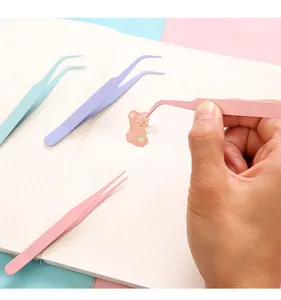 Primer plano de unas pinzas curvas de acero rosa recogiendo una pegatina de osito