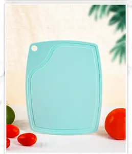 Detail view of a mint green plastic PP cutting board featuring a juice groove and hanging hole