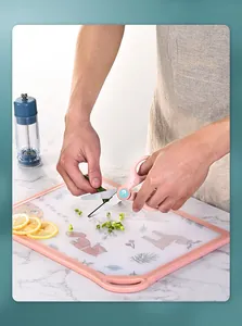 Close-up of a pink cartoon cutting board being used to chop fresh green scallions