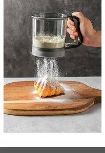 Handheld semi-automatic flour sifter dusting a croissant on a wooden cutting board detail