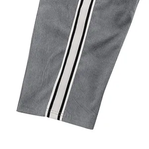 Close-up detail of grey corduroy trousers showing side stripe tape and fabric texture.