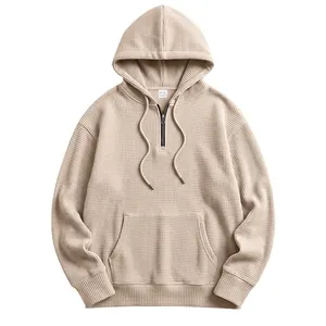 Detail of beige waffle knit hoodie with half-zip and kangaroo pocket design.