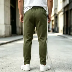 Back view of men's olive green sweatpants with white side stripes in street setting.