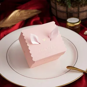 Close-up of pink square wedding favor candy box with decorative ribbon ears and gold