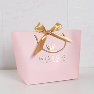 Detailed view of elegant pink gift paper bag with gold ribbon bow and rope handle
