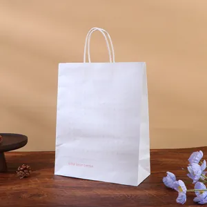 White paper gift bag with handles on a wooden table with decorative flowers