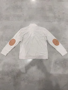 Detail of ribbed long-sleeved sweatshirt with brown elbow patches on grey floor