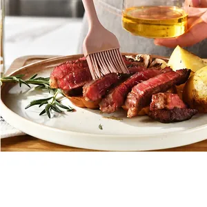 Nahaufnahme eines Silikon-Backpinsels, der Öl auf Steak und Kartoffeln streicht