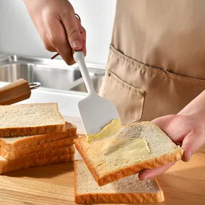 Premium white silicone spatula with acacia wood handle spreading butter on fresh toast.