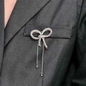 Detailed view of an elegant silver metal bowknot brooch with dangling tassels on a suit pocket.