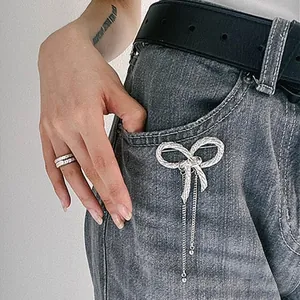 Detail of a silver metallic bow brooch with long tassels pinned to a grey denim pocket