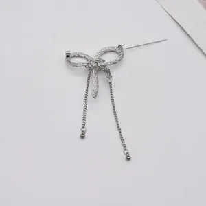 Detailed view of a silver textured metal bow brooch with elegant hanging tassel chains.