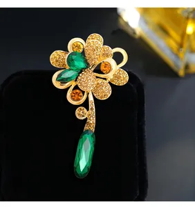 Macro detail of an elegant gold flower brooch with green and amber crystal gems.