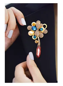 Macro view of a gold-plated flower brooch featuring vibrant crystals and a teardrop pendant