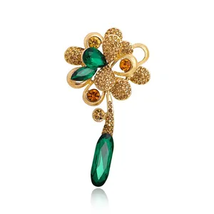 Elegant gold flower brooch decorated with green crystals and a teardrop tassel accent.
