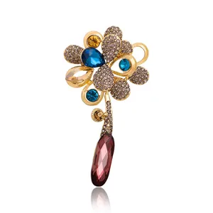 Elegant gold-toned flower brooch featuring blue rhinestones and a large brown crystal drop