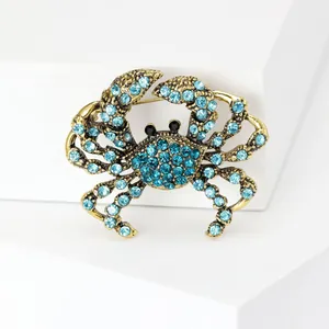 Detailansicht einer goldfarbenen Krabbenbrosche mit blauen Kristallen auf weiß.