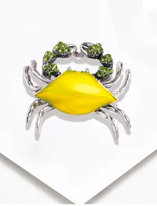 Close-up of a crab brooch with yellow enamel shell and sparkling green rhinestones on white surface.