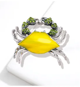 Detailed macro view of a silver crab brooch with yellow enamel and green rhinestones.