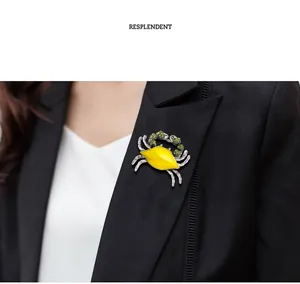 Detail view of a yellow enamel crab brooch with green rhinestones on a black blazer