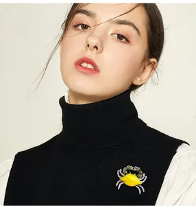Detailed view of yellow enamel crab brooch with green rhinestones on a black turtleneck sweater