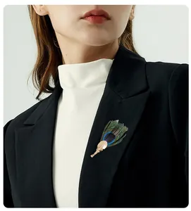 Elegant handmade peacock feather brooch pin worn on a black blazer lapel detail view.
