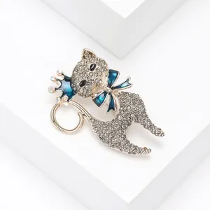 Dettaglio macro di una spilla a gatto con strass, fiocco blu e corona scintillante.