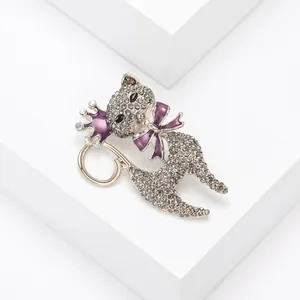 Vista dettagliata di un'elegante spilla a gatto con strass, corona e fiocco viola scuro