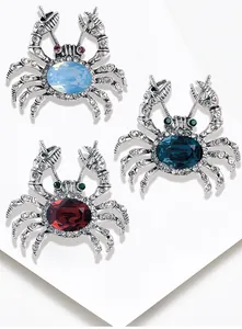 Set of sparkling alloy crab brooches with blue and red oval gemstones on a white surface
